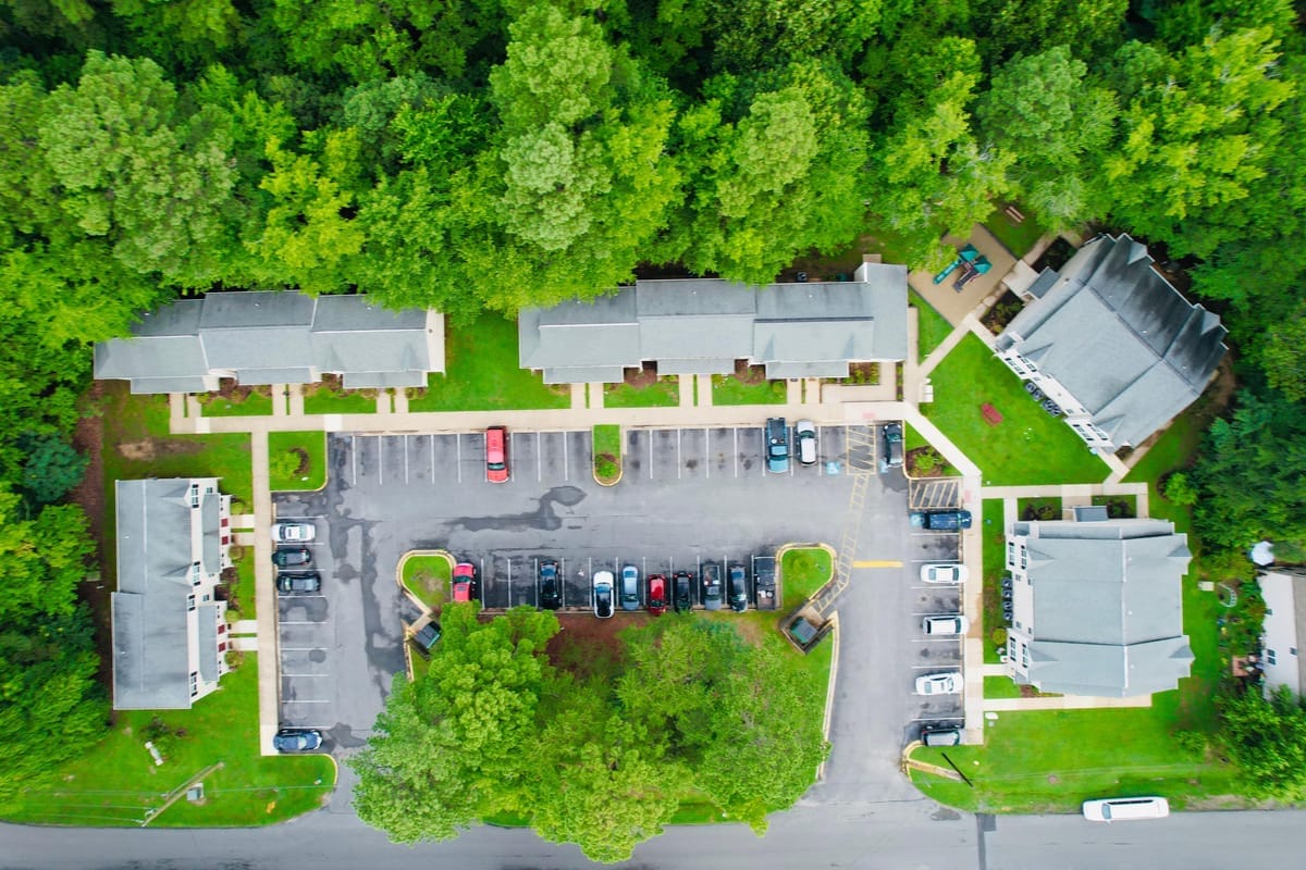 Overhead aerial of the entire Colonial Beach Village property, with rows of buildings, a parking lot, walkways, and lawns surrounded by woods