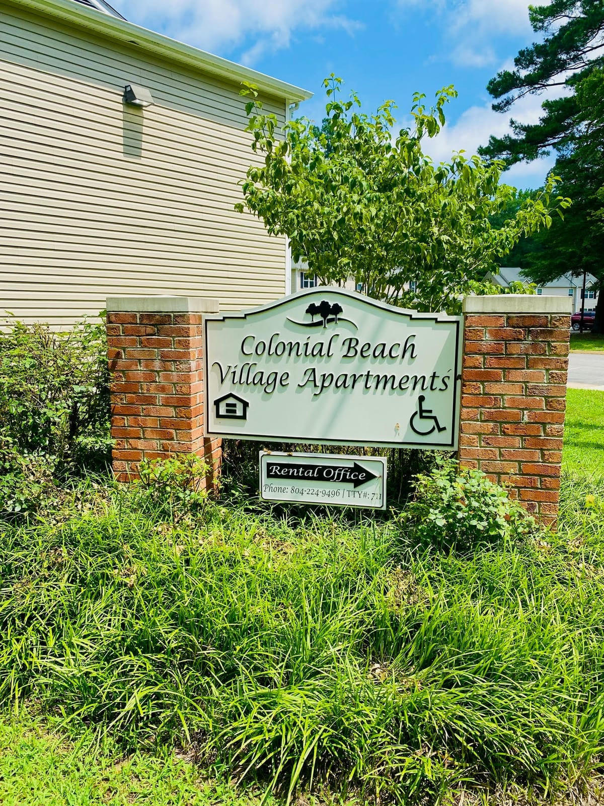 The Colonial Beach Village Apartments monument sign on brick posts, with a rental-office arrow and the leasing phone number below